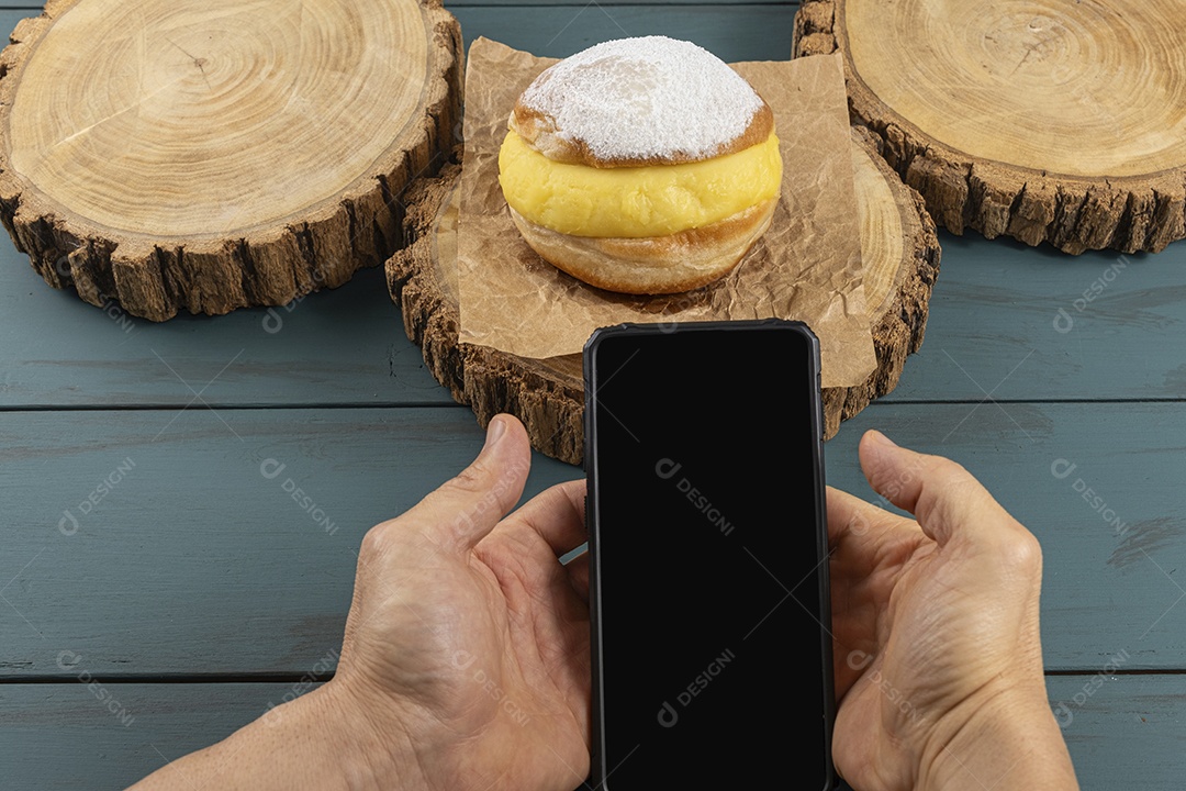 Doce sonho creme sobre tábua de madeira e pessoa com celular nas mão