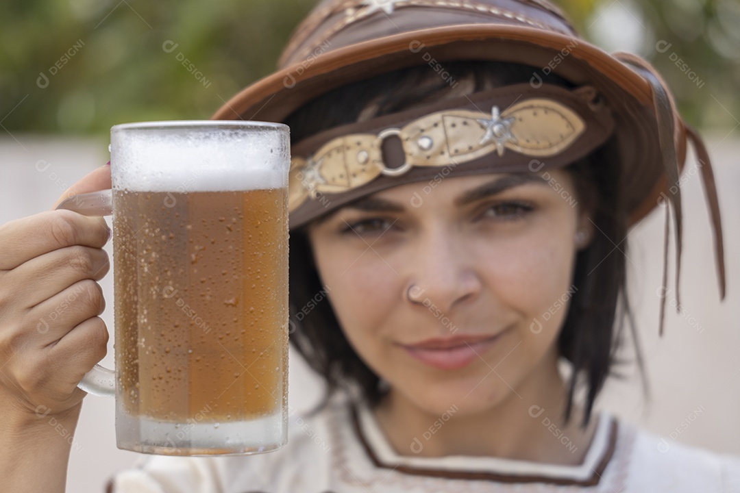 Jovem vestindo fantasia típica de festa junina segurando uma caneca de cerveja gelada