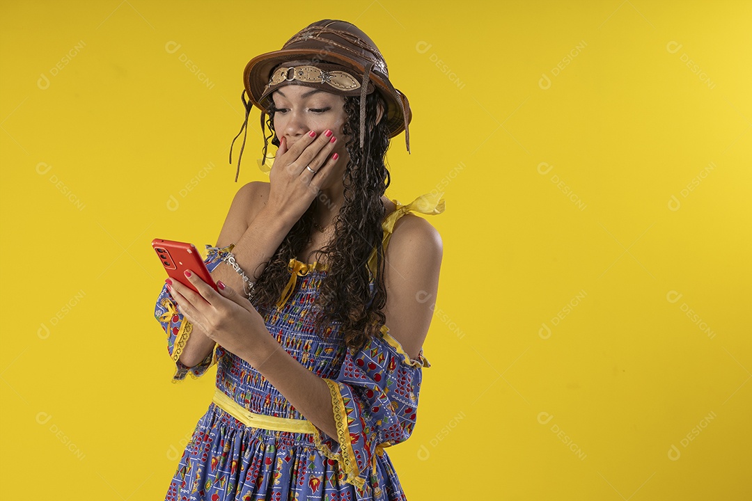 Jovem sorrindo com celular na mão e trajes de festa junina