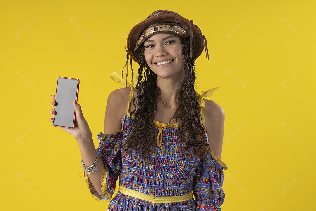 Jovem sorrindo com celular na mão e trajes de festa junina