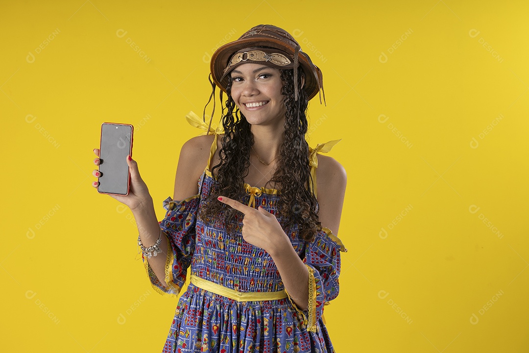 Jovem sorrindo com celular na mão e trajes de festa junina