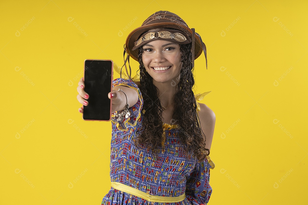Jovem sorrindo com celular na mão e trajes de festa junina