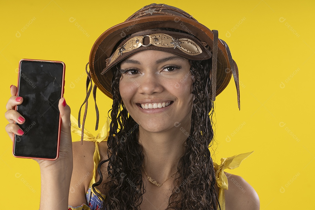 Jovem sorrindo com celular na mão e trajes de festa junina