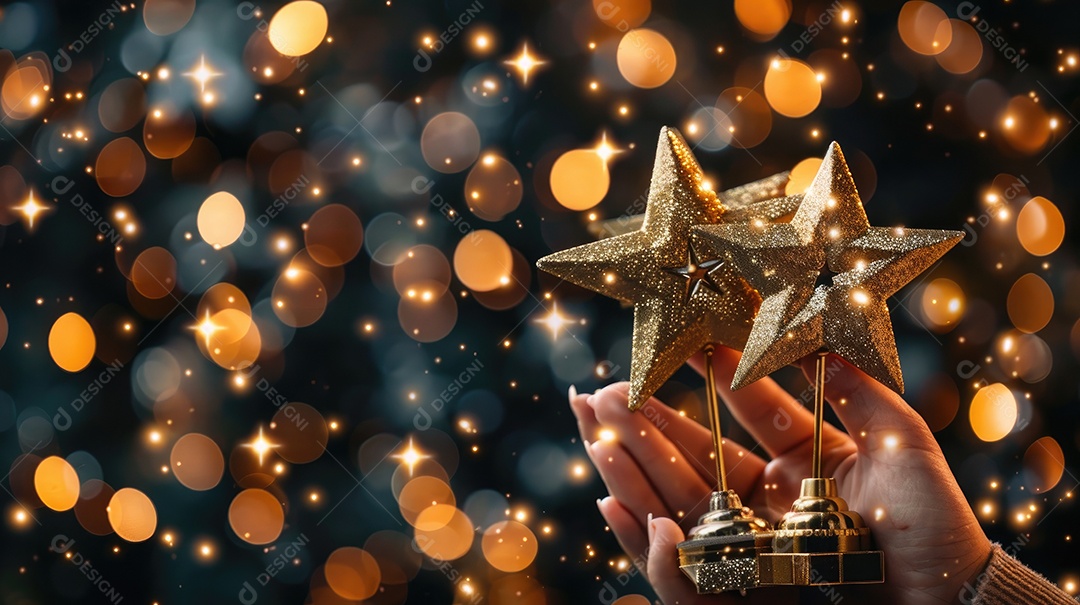 Um close de uma mão segurando cinco prêmios de estrelas douradas cada um brilhando sob uma iluminação suave e focada.