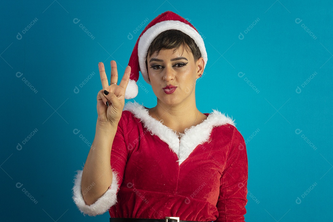 Mulher jovem com roupa de Mamãe Noel e chapéu com gesto de três dedo