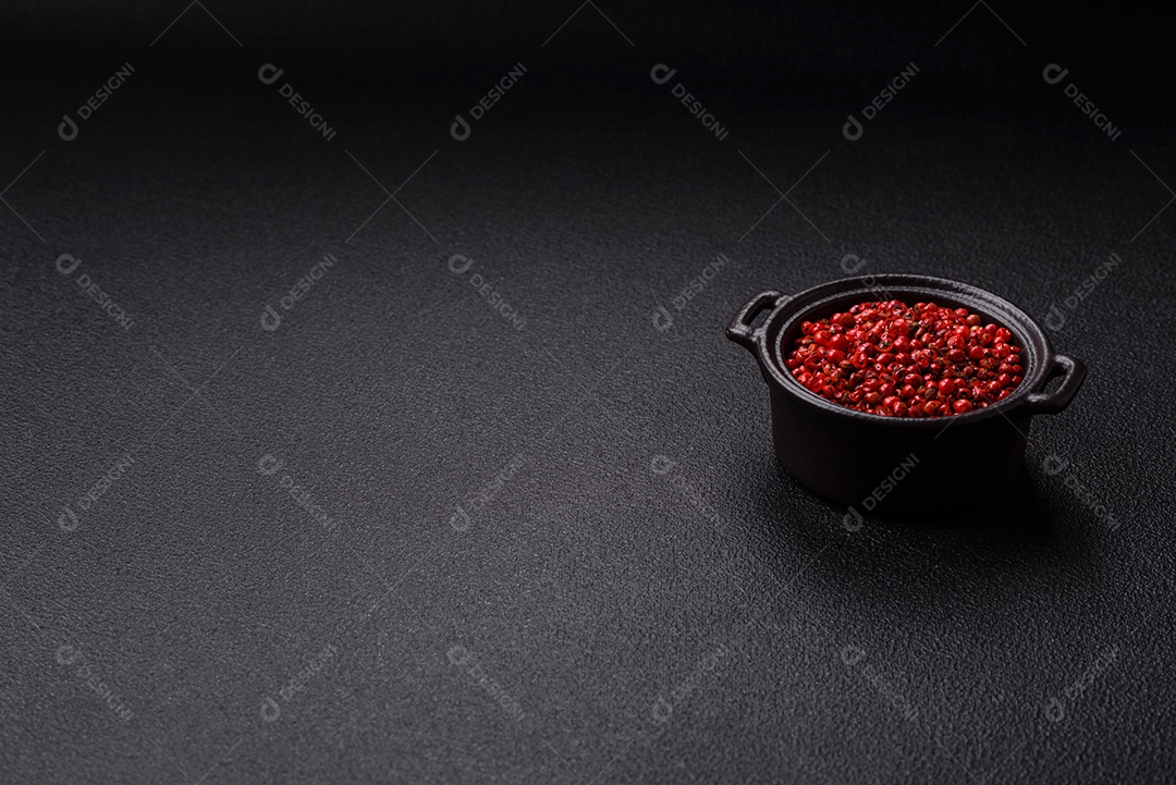 Especiarias, ervilhas de pimenta da Jamaica na cor vermelha ou rosa em uma tigela sobre um fundo preto de concreto. Cozinha asiática