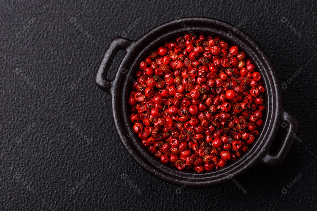 Especiarias, ervilhas de pimenta da Jamaica na cor vermelha ou rosa em uma tigela sobre um fundo preto de concreto. Cozinha asiática