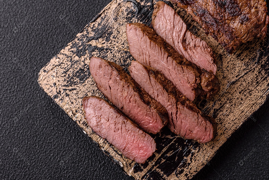 Bife fresco, suculento e delicioso em um fundo escuro. Prato de carne com especiarias e ervas