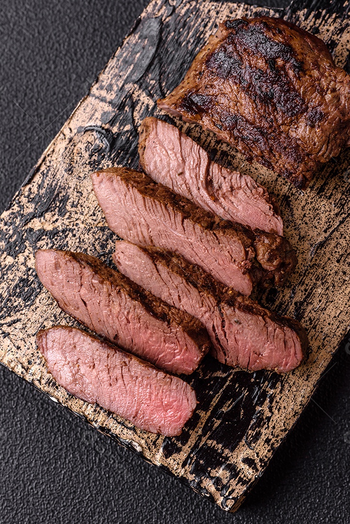 Bife suculento de tomahawk com osso assado na grelha com sal e especiarias em um fundo escuro de concreto