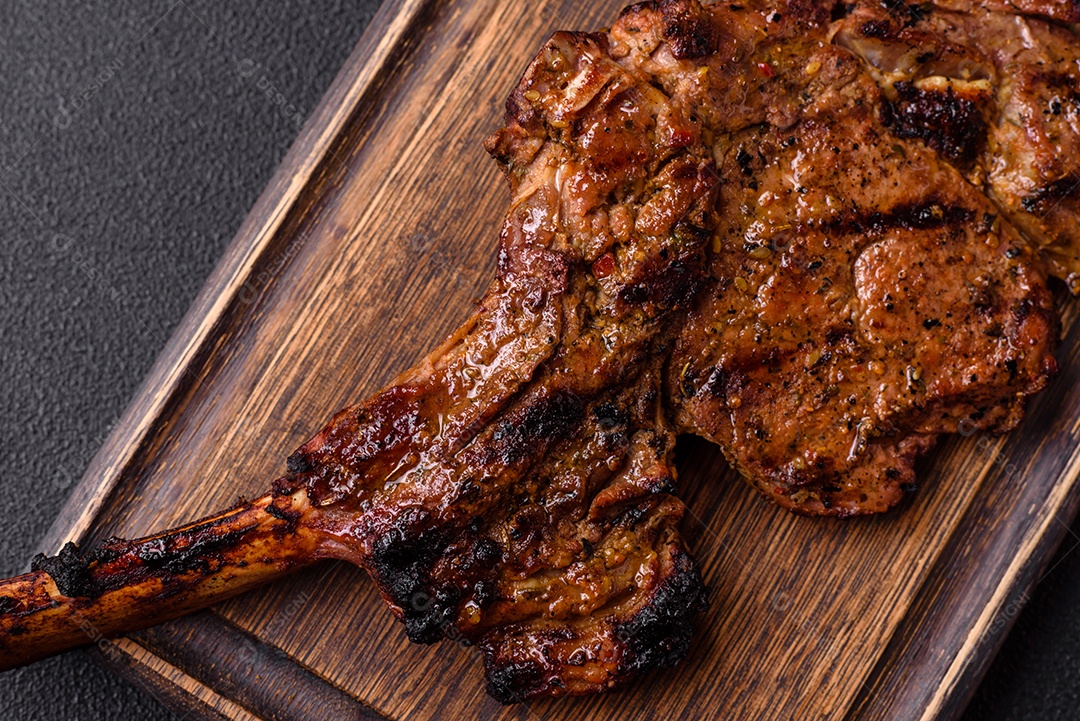 Bife suculento de tomahawk com osso assado na grelha com sal e especiarias em um fundo escuro de concreto