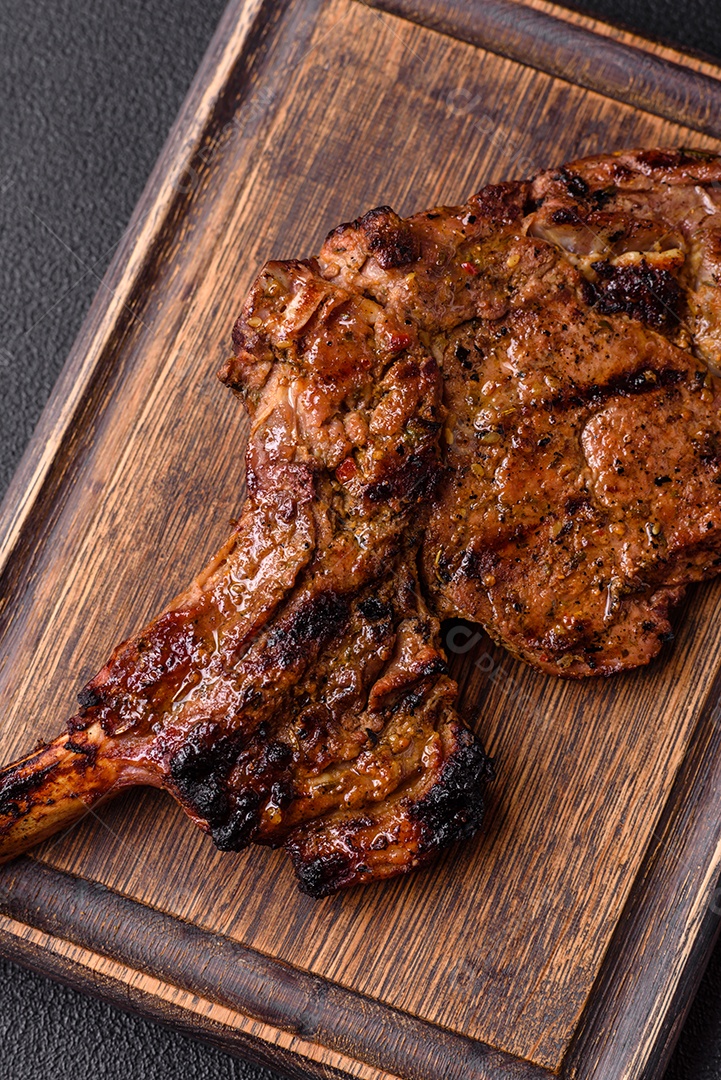 Bife suculento de tomahawk com osso assado na grelha com sal e especiarias em um fundo escuro de concreto