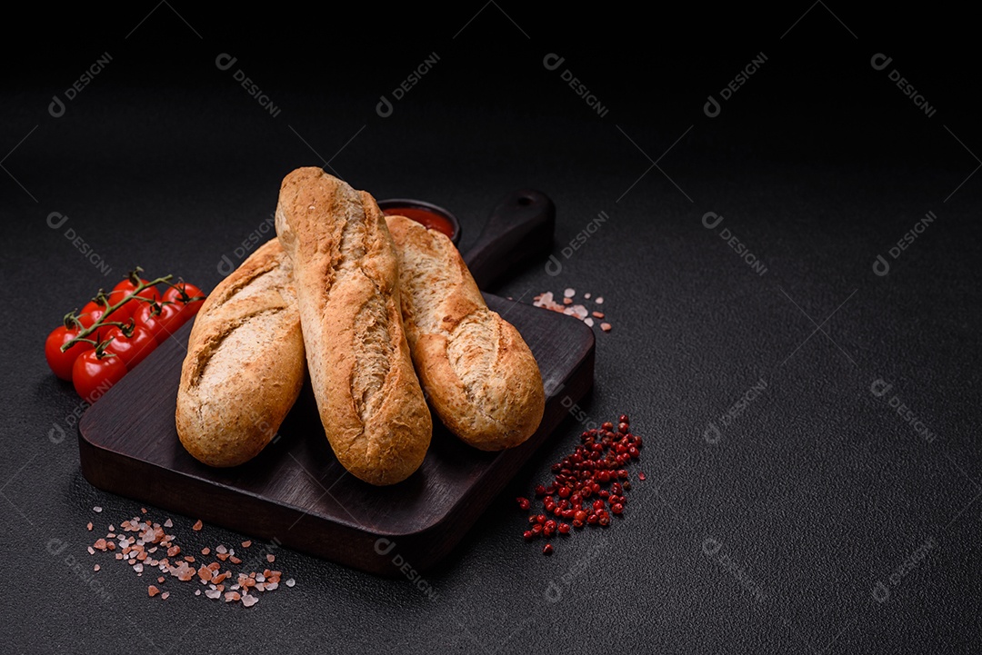 Mini baguete crocante com sementes e grãos, sal e especiarias sobre fundo escuro de concreto