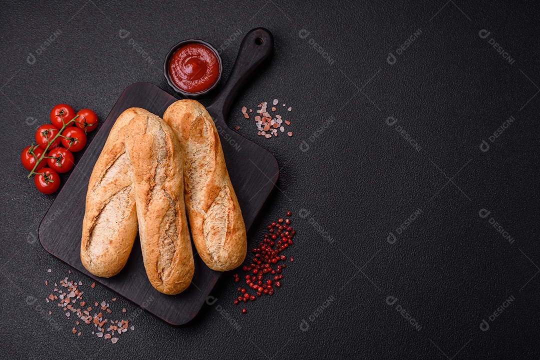 Mini baguete crocante com sementes e grãos, sal e especiarias sobre fundo escuro de concreto