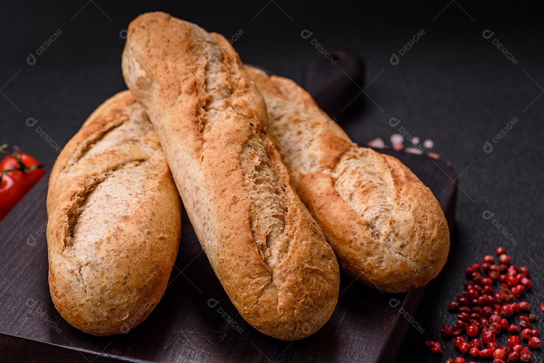 Mini baguete crocante com sementes e grãos, sal e especiarias sobre fundo escuro de concreto