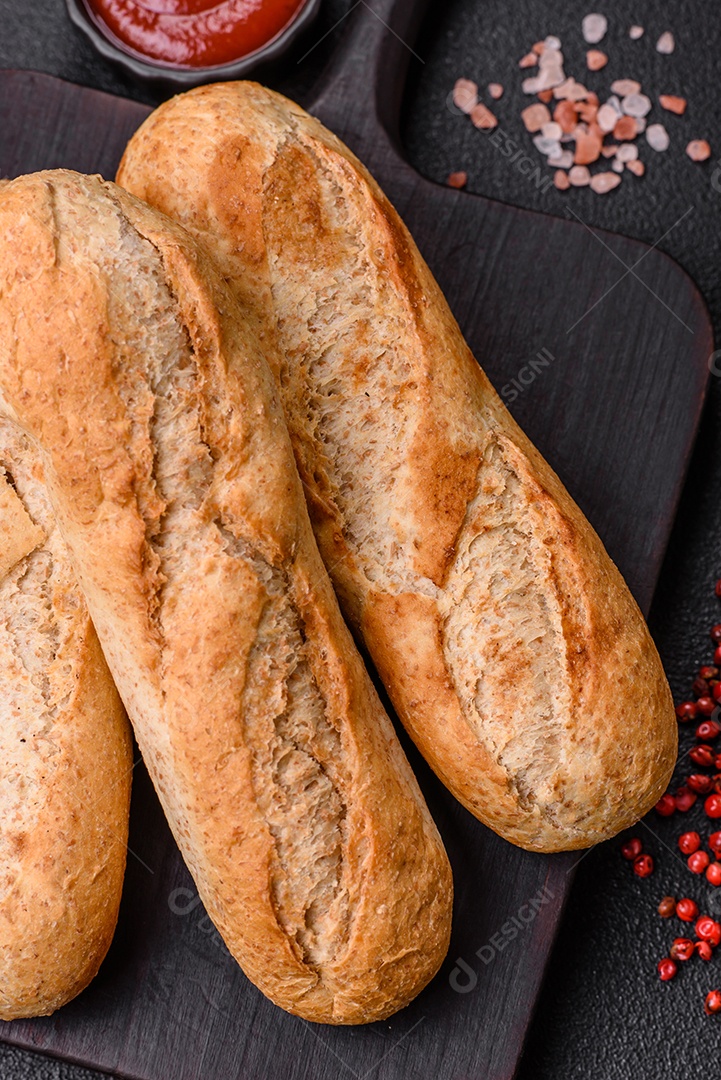 Mini baguete crocante com sementes e grãos, sal e especiarias sobre fundo escuro de concreto