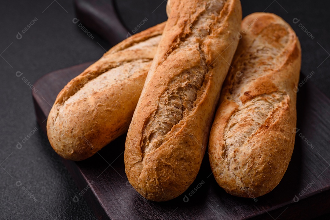 Mini baguete crocante com sementes e grãos, sal e especiarias sobre fundo escuro de concreto