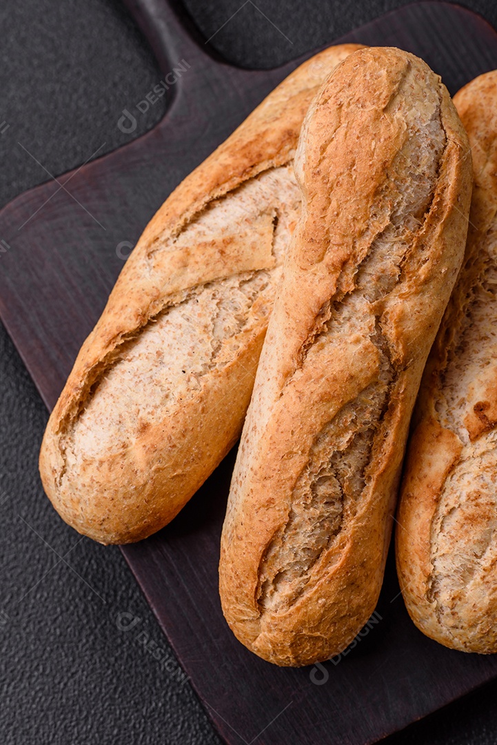 Mini baguete crocante com sementes e grãos, sal e especiarias sobre fundo escuro de concreto