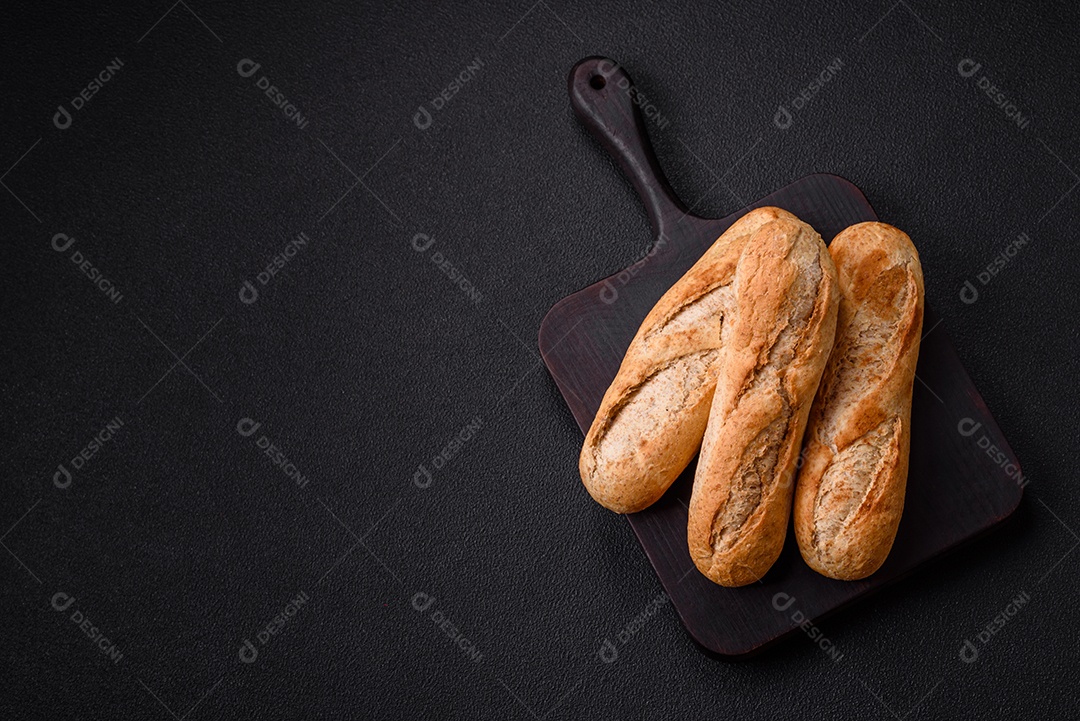 Mini baguete crocante com sementes e grãos, sal e especiarias sobre fundo escuro de concreto