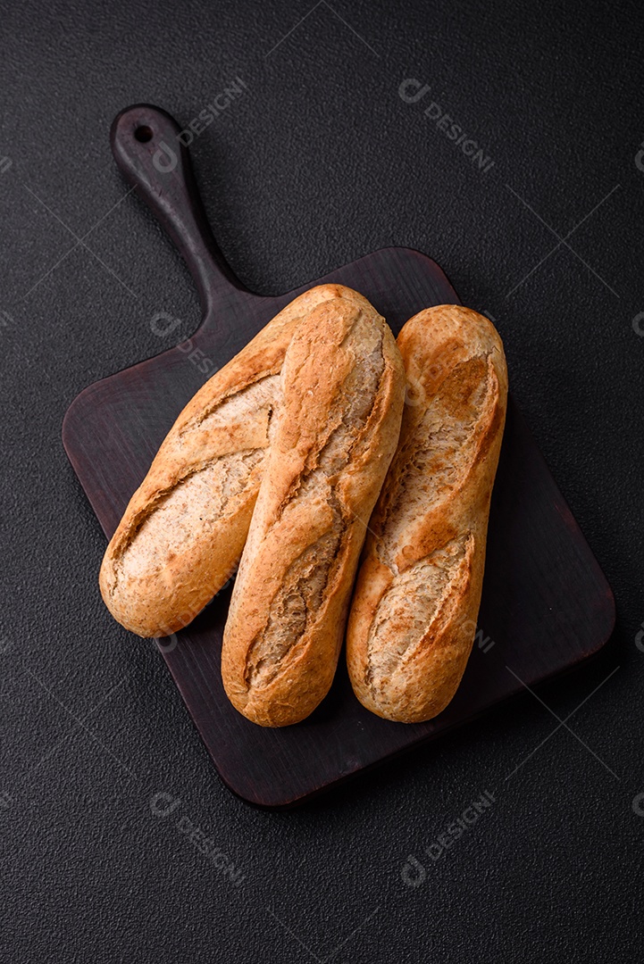 Mini baguete crocante com sementes e grãos, sal e especiarias sobre fundo escuro de concreto