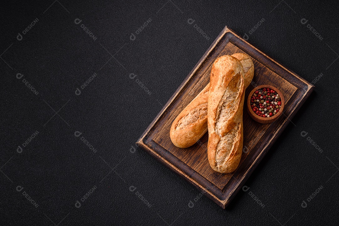 Mini baguete crocante com sementes e grãos, sal e especiarias sobre fundo escuro de concreto