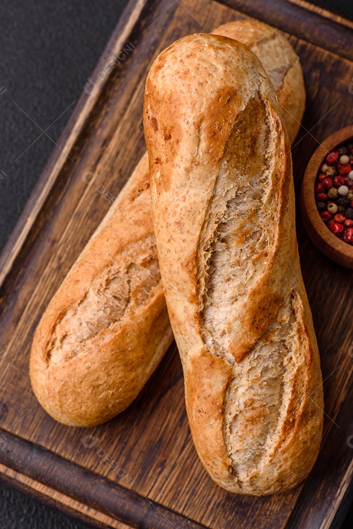 Mini baguete crocante com sementes e grãos, sal e especiarias sobre fundo escuro de concreto