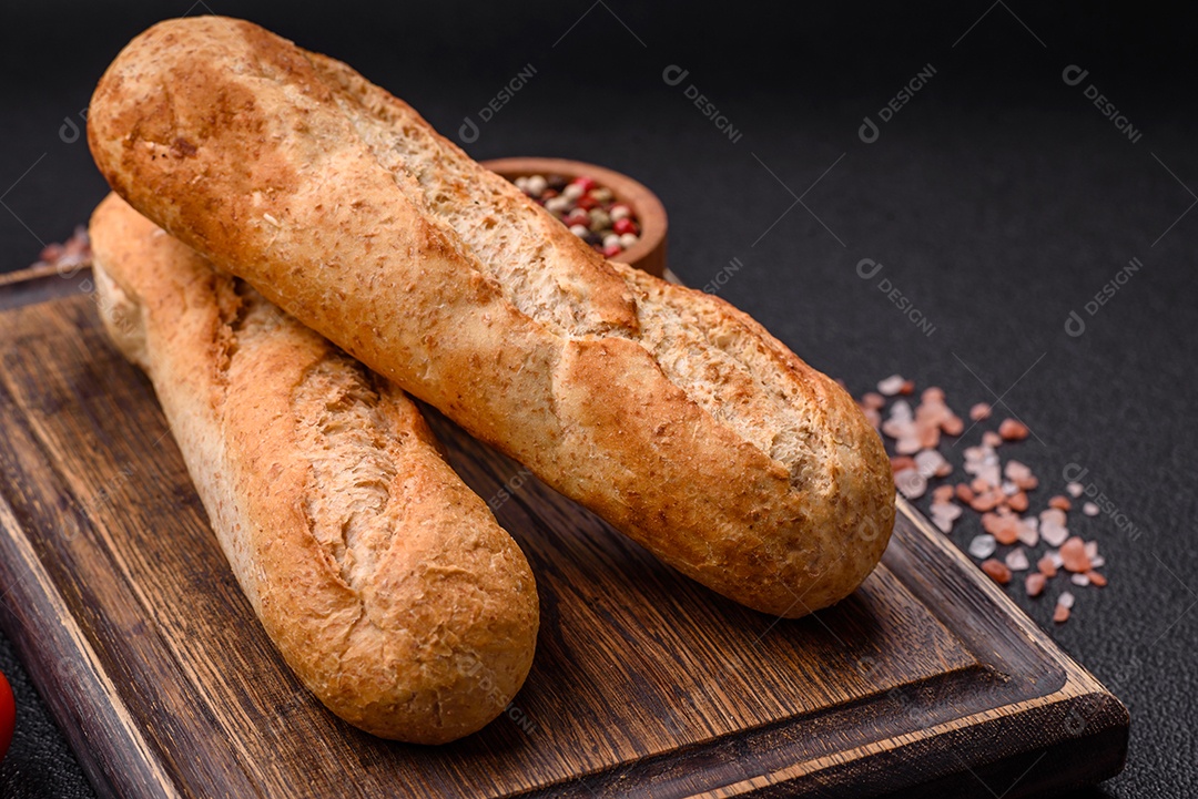 Mini baguete crocante com sementes e grãos, sal e especiarias sobre fundo escuro de concreto