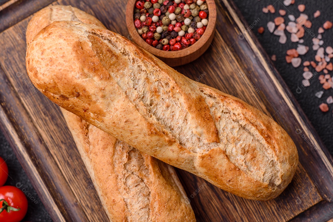 Mini baguete crocante com sementes e grãos, sal e especiarias sobre fundo escuro de concreto