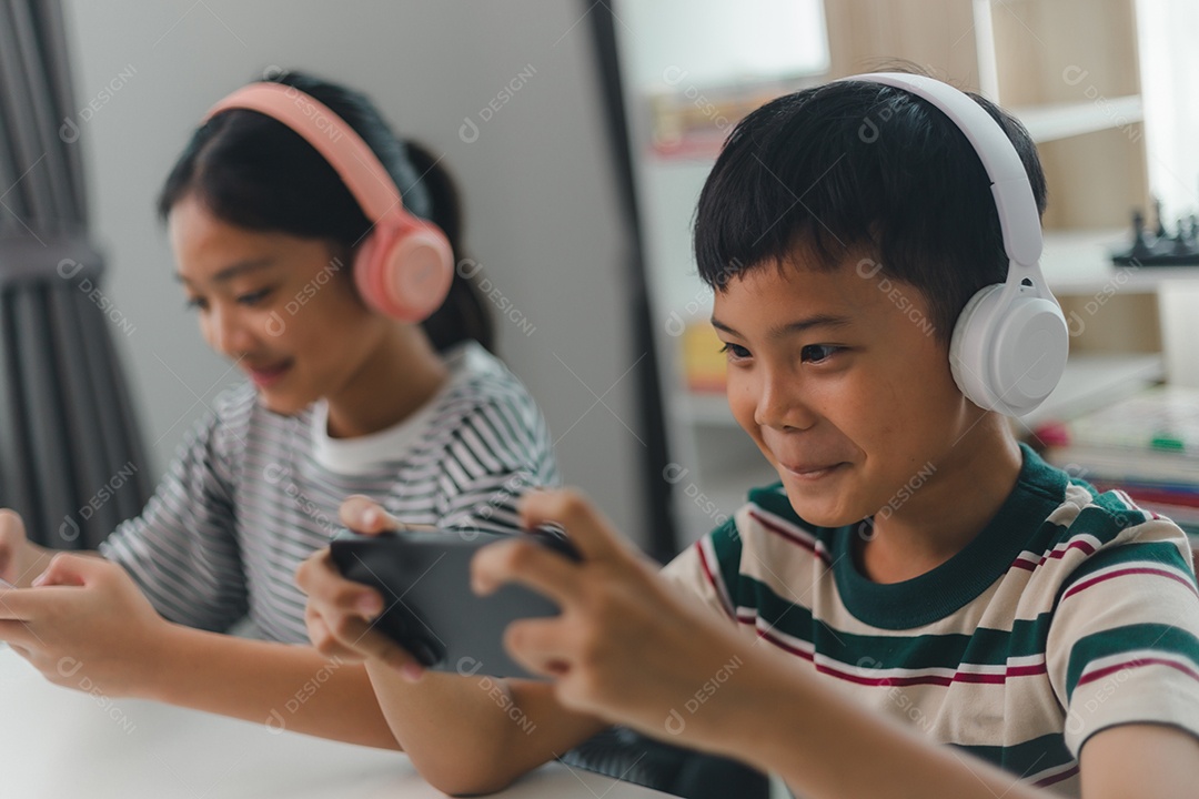 Crianças asiáticas jogam videogame online com amigos em celulares para se divertir em casa