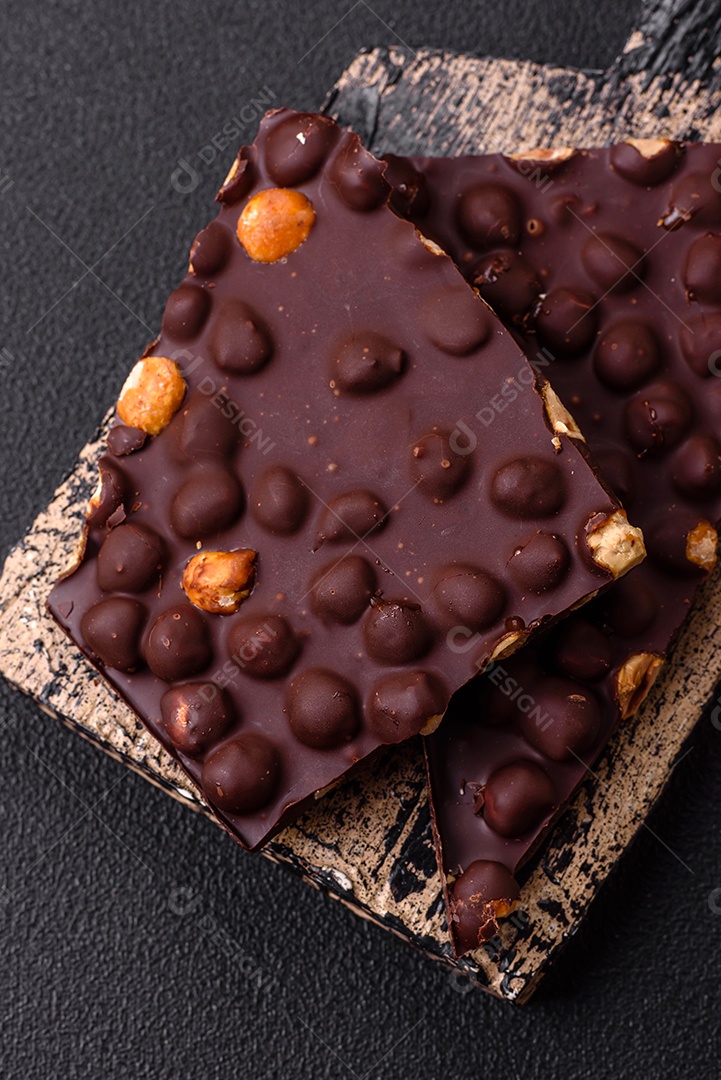 Chocolate amargo preto com avelãs inteiras, frutas cristalizadas e hortelã, quebrado em pedaços sobre fundo escuro de concreto