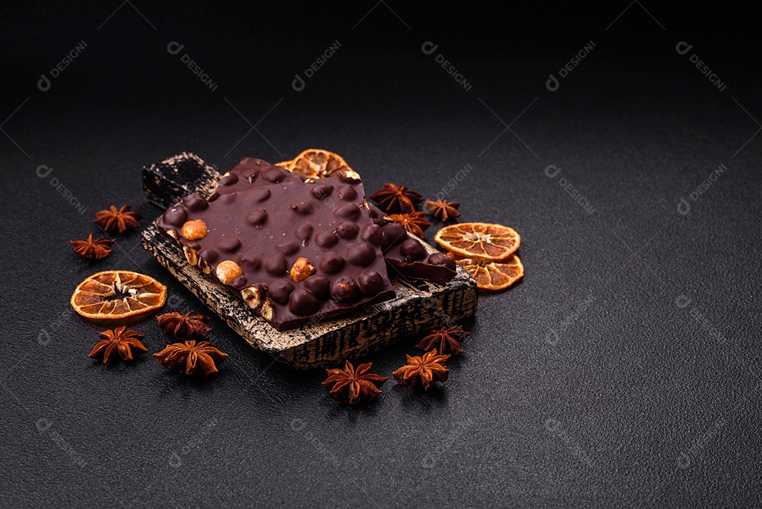 Chocolate amargo preto com avelãs inteiras, frutas cristalizadas e hortelã, quebrado em pedaços sobre fundo escuro de concreto