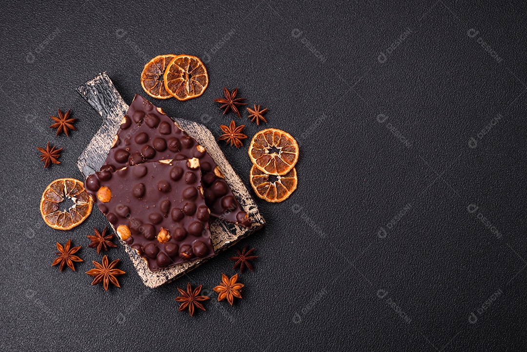 Chocolate amargo preto com avelãs inteiras, frutas cristalizadas e hortelã, quebrado em pedaços sobre fundo escuro de concreto