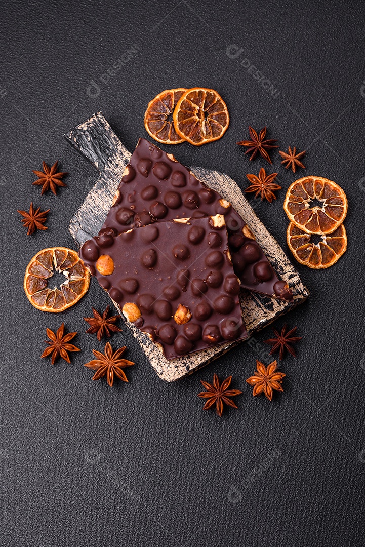 Chocolate amargo preto com avelãs inteiras, frutas cristalizadas e hortelã, quebrado em pedaços sobre fundo escuro de concreto