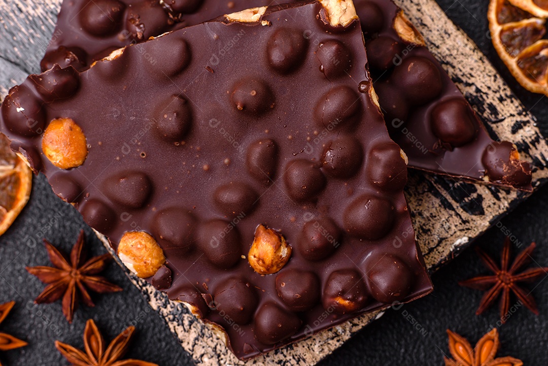 Chocolate amargo preto com avelãs inteiras, frutas cristalizadas e hortelã, quebrado em pedaços sobre fundo escuro de concreto