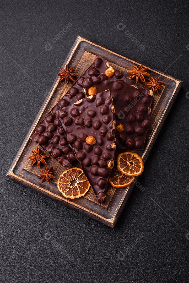 Chocolate amargo preto com avelãs inteiras, frutas cristalizadas e hortelã, quebrado em pedaços sobre fundo escuro de concreto