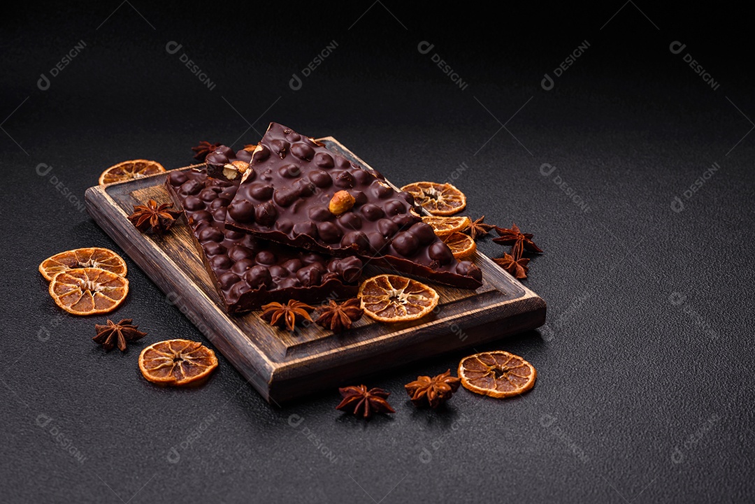 Chocolate amargo preto com avelãs inteiras, frutas cristalizadas e hortelã, quebrado em pedaços sobre fundo escuro de concreto