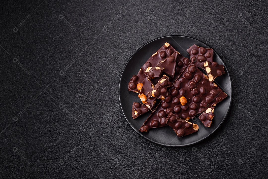 Chocolate amargo preto com avelãs inteiras, frutas cristalizadas e hortelã, quebrado em pedaços sobre fundo escuro de concreto