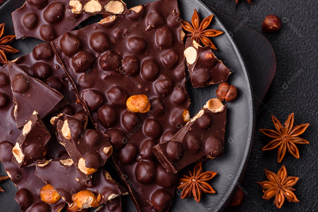 Chocolate amargo preto com avelãs inteiras, frutas cristalizadas e hortelã, quebrado em pedaços sobre fundo escuro de concreto