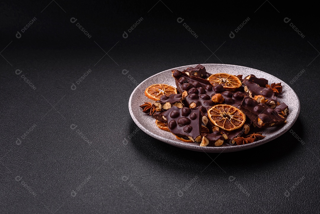 Chocolate amargo preto com avelãs inteiras, frutas cristalizadas e hortelã, quebrado em pedaços sobre fundo escuro de concreto