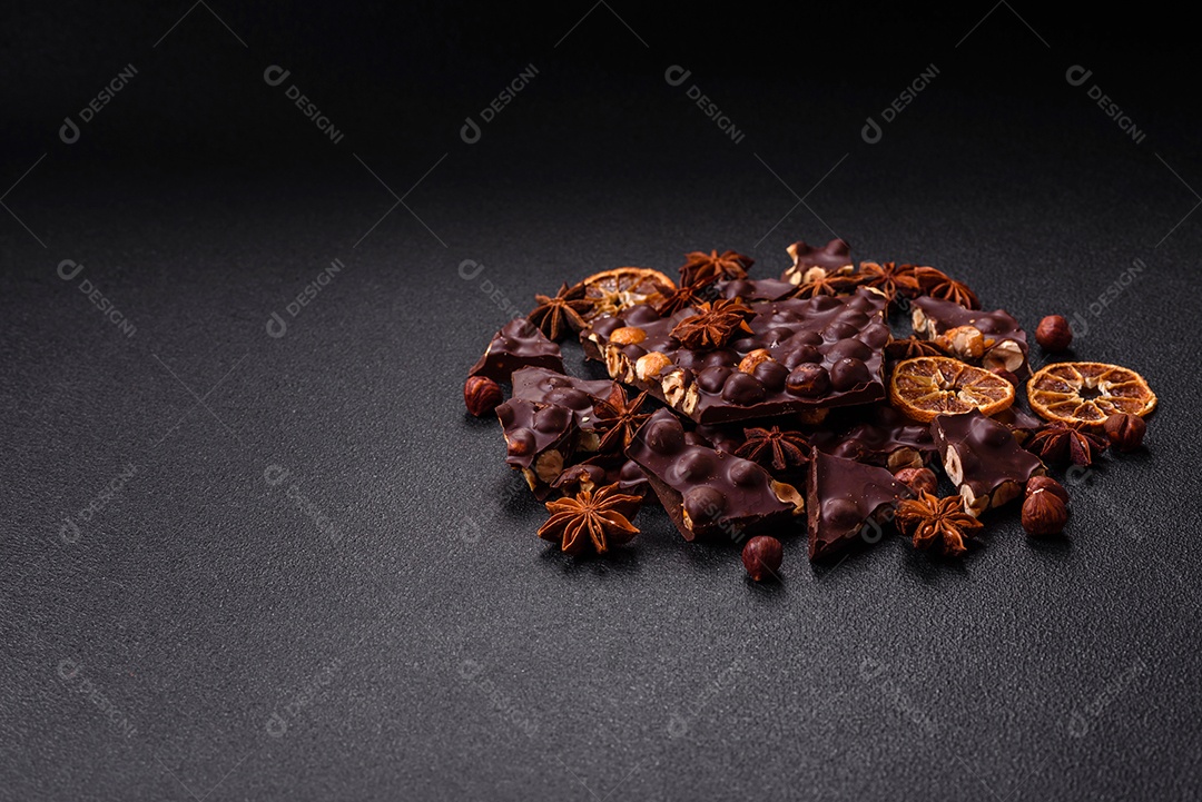 Chocolate amargo preto com avelãs inteiras, frutas cristalizadas e hortelã, quebrado em pedaços sobre fundo escuro de concreto