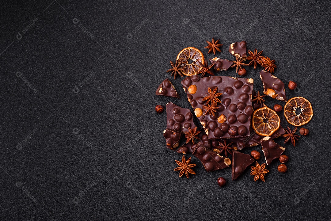 Chocolate amargo preto com avelãs inteiras, frutas cristalizadas e hortelã, quebrado em pedaços sobre fundo escuro de concreto
