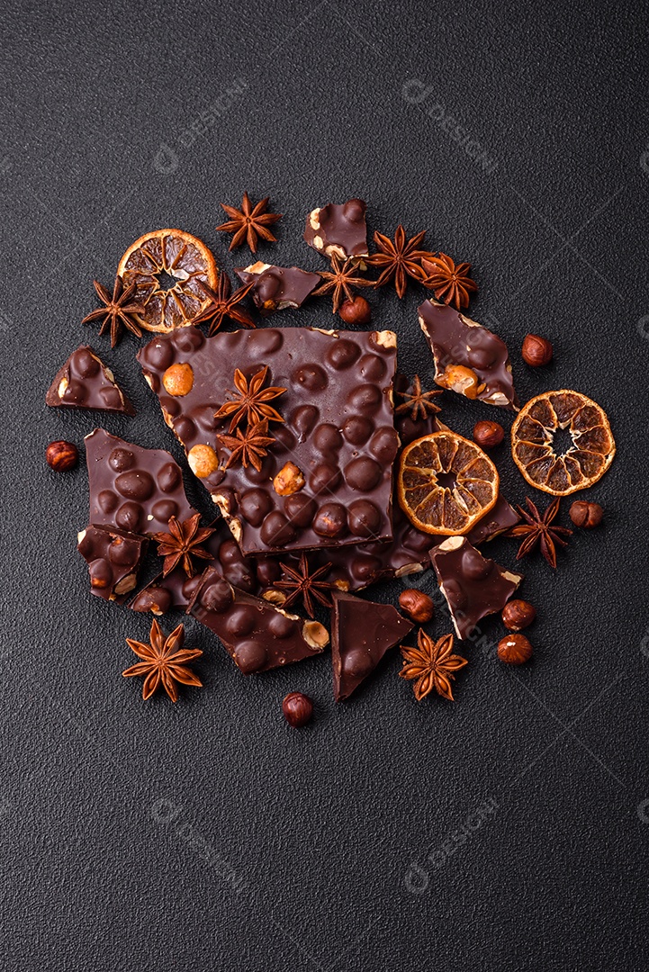 Chocolate amargo preto com avelãs inteiras, frutas cristalizadas e hortelã, quebrado em pedaços sobre fundo escuro de concreto