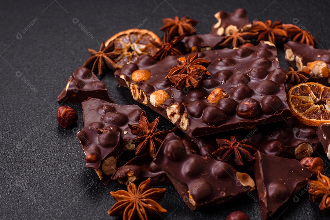 Chocolate amargo preto com avelãs inteiras, frutas cristalizadas e hortelã, quebrado em pedaços sobre fundo escuro de concreto