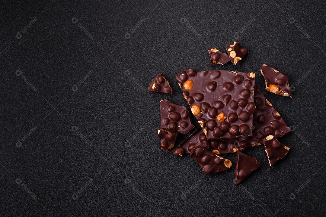 Chocolate amargo preto com avelãs inteiras, frutas cristalizadas e hortelã, quebrado em pedaços sobre fundo escuro de concreto