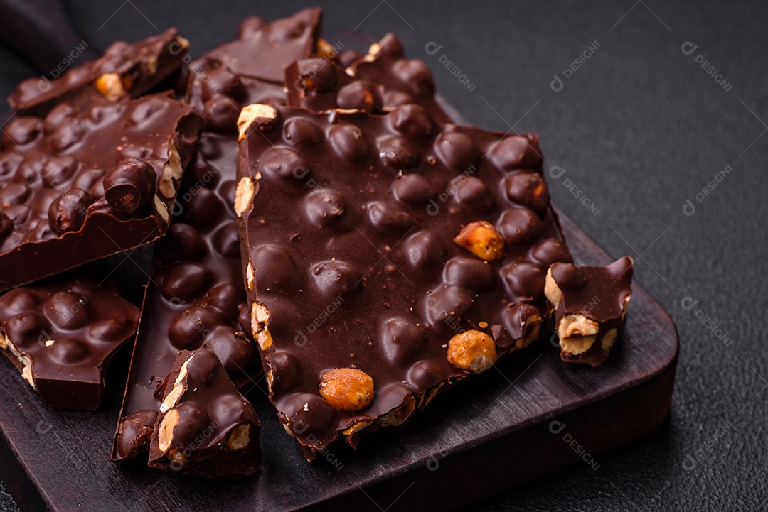 Chocolate amargo preto com avelãs inteiras, frutas cristalizadas e hortelã, quebrado em pedaços sobre fundo escuro de concreto