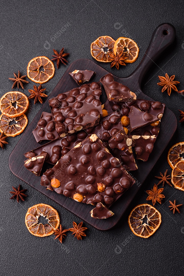Chocolate amargo preto com avelãs inteiras, frutas cristalizadas e hortelã, quebrado em pedaços sobre fundo escuro de concreto