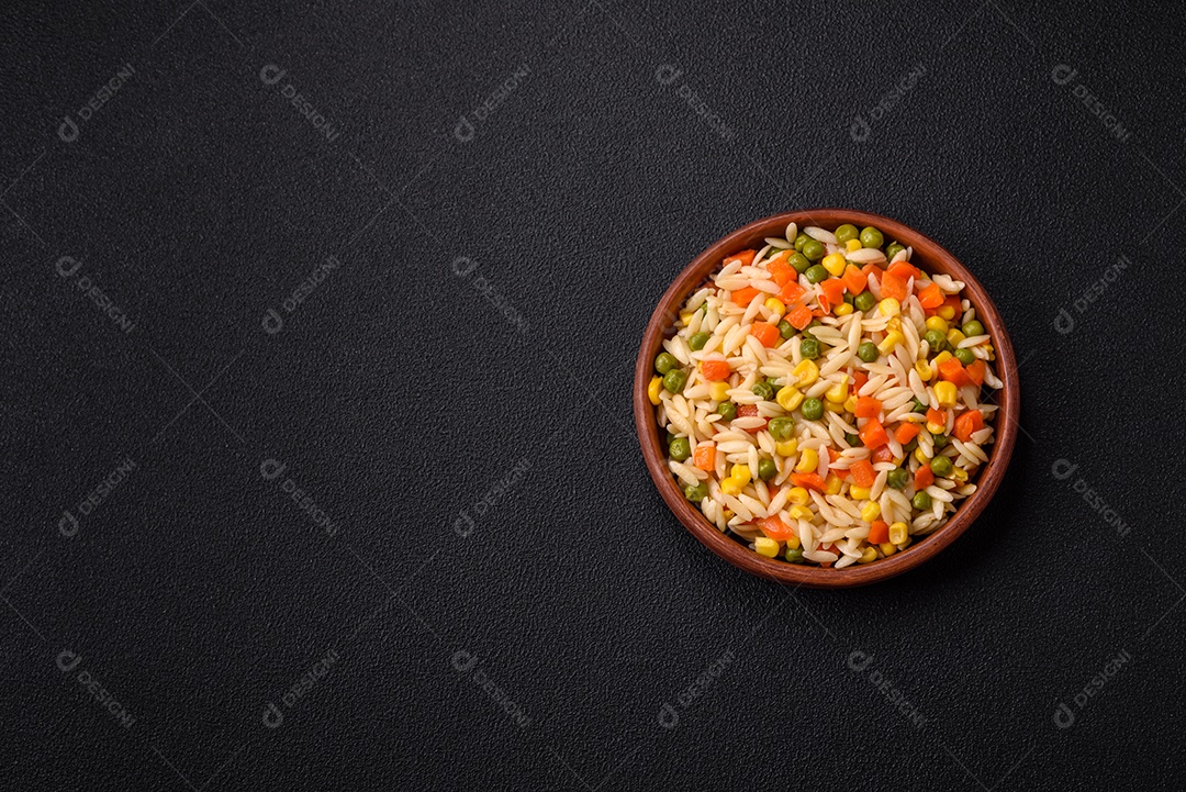 Delicioso arroz cozido com legumes milho, cenouras, ervilhas com sal, especiarias e ervas sobre um fundo escuro de concreto