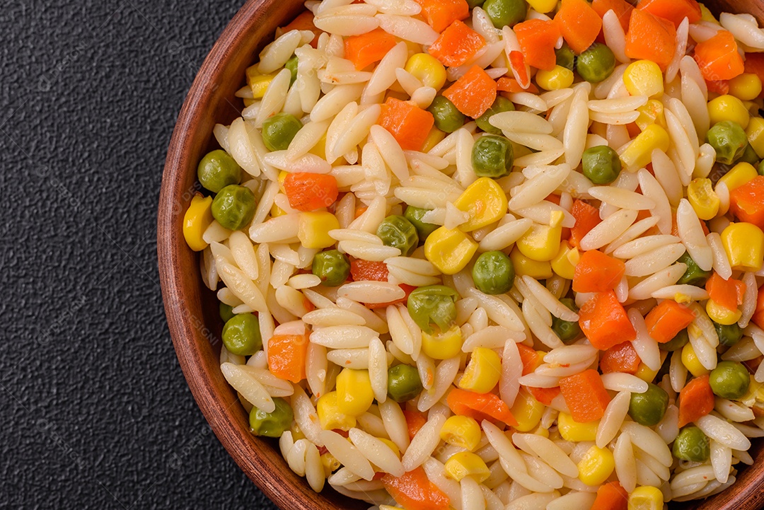 Delicioso arroz cozido com legumes milho, cenouras, ervilhas com sal, especiarias e ervas sobre um fundo escuro de concreto