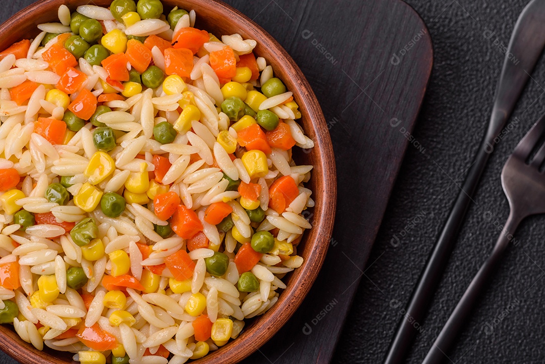 Delicioso arroz cozido com legumes milho, cenouras, ervilhas com sal, especiarias e ervas sobre um fundo escuro de concreto