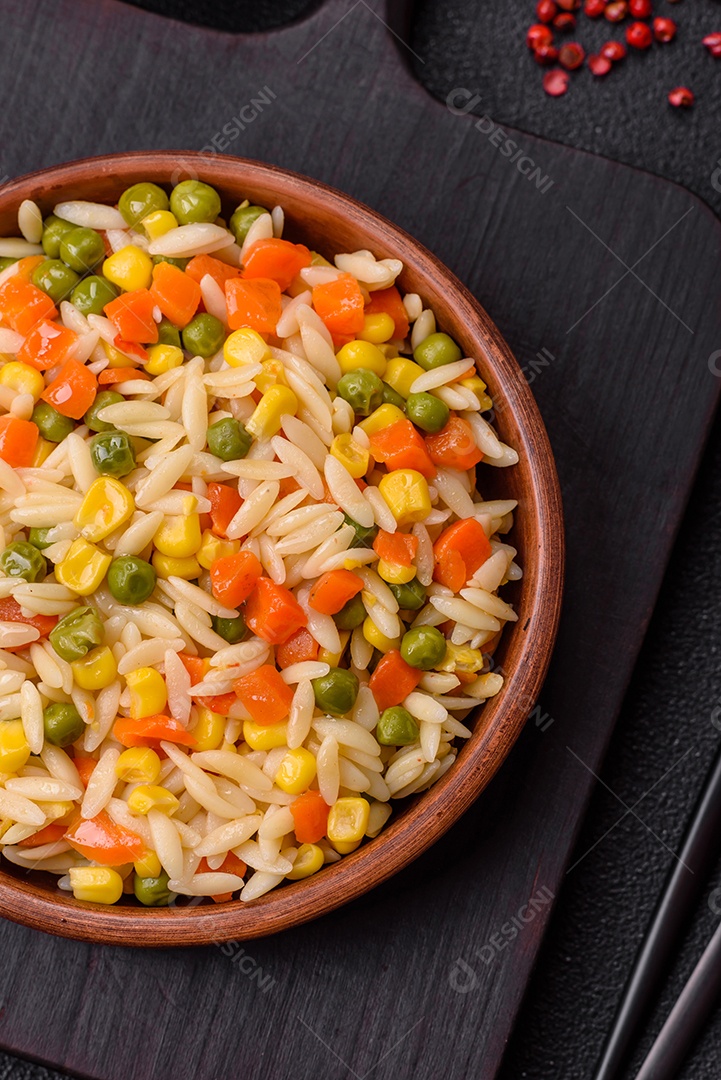 Delicioso arroz cozido com legumes milho, cenouras, ervilhas com sal, especiarias e ervas sobre um fundo escuro de concreto