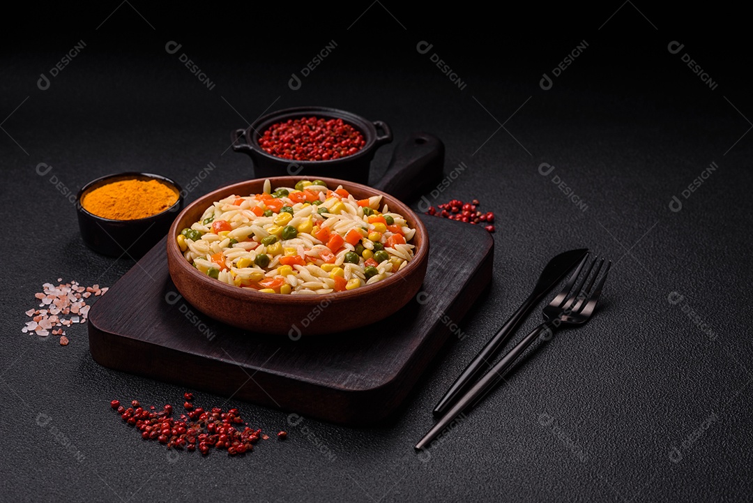 Delicioso arroz cozido com legumes milho, cenouras, ervilhas com sal, especiarias e ervas sobre um fundo escuro de concreto